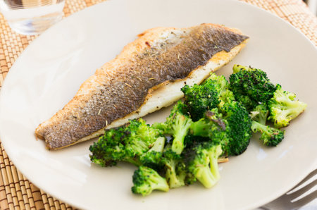 fried fillet of sea bass with garnish of broccoli on black warm stone plateの写真素材