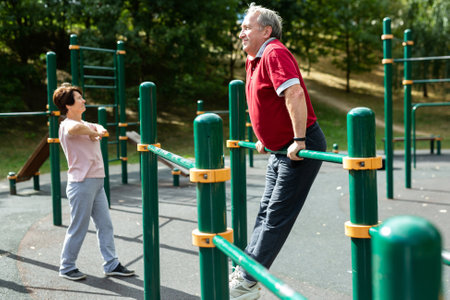 Aged man doing exercises on sports bars in open-air sports area