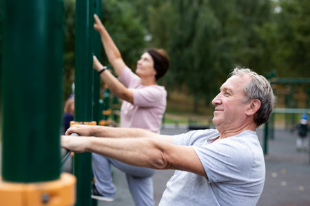 Aged man doing exercises on sports bars in open-air sports area