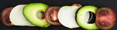 chopped vegetables black tomatoes, avocado and onions against black stone boardの写真素材