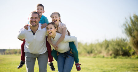 happy family of parents with two children enjoy a walk in city parkの写真素材