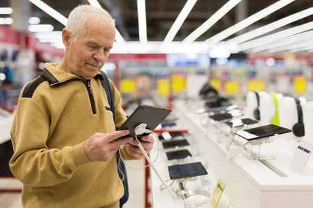 elderly man examines tablet computer in showroom of electronics storeの写真素材