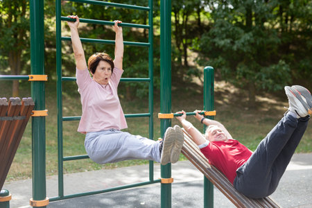 Mature woman goes in for sports in city park on sports ground - doing exercises to pull his legs to...