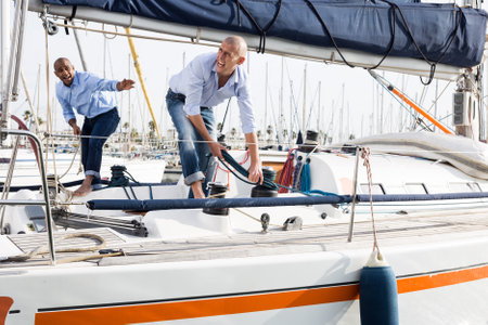 Two young men in blue shirts tidy up private sailing yacht in the seaportの写真素材