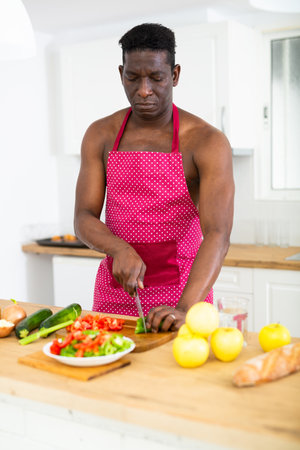 Man with a naked torso in an apron prepares a vegetable salad in the kitchenの写真素材