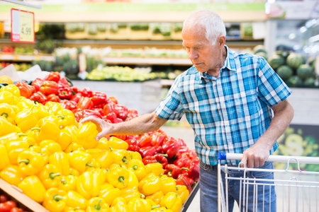 Elderly retired man buying bell pepper in grocery section of supermarketの写真素材