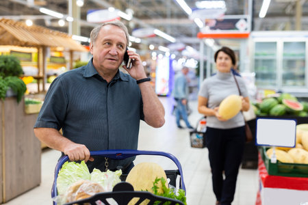 Elderly man talking on mobile phone in supermarketの写真素材