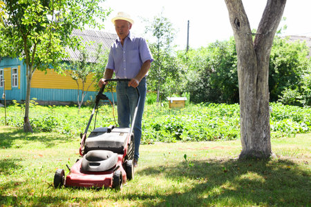 Elderly man with a lawn mower while mowing the lawnの写真素材