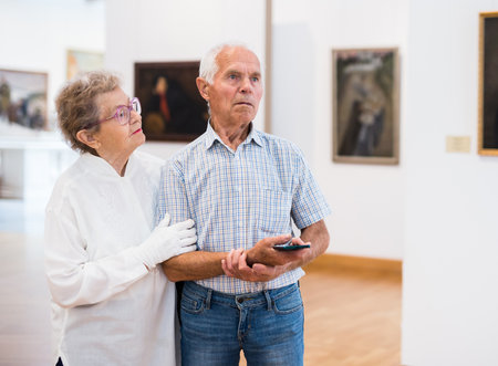 Mature European couple examines paintings in an exhibition in hall of art museumの写真素材