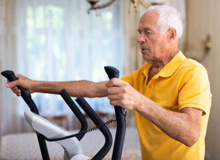 Old man using elliptic trainer at homeの写真素材