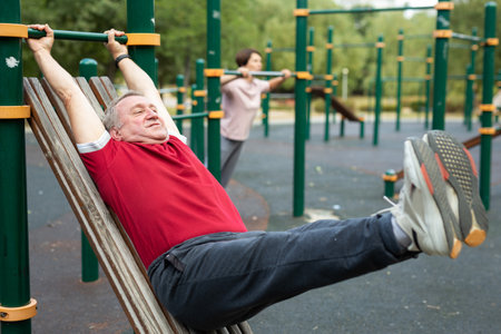 Senior man goes in for sports in city park on sports ground - doing exercises to pull his legs to...