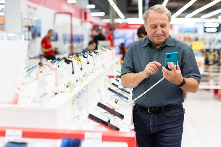 Elderly man chooses mobile phone in storeの写真素材