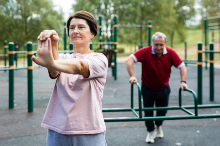 Elderly woman does gymnastics on an outdoor sports ground