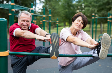 Elderly man and woman doing exercises in sports bars on outdoor sports ground