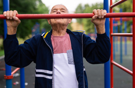 Sportive old man doing pull-ups outdoors