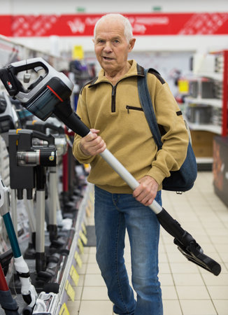 Senor man pensioner buying Upright Vacuum Cleaner in showroom of electrical appliance storeの写真素材
