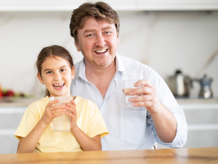 Father and little daughter drink water from glasses in home kitchenの写真素材