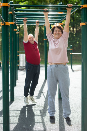 Elderly man and woman doing exercises in sports bars on outdoor sports ground