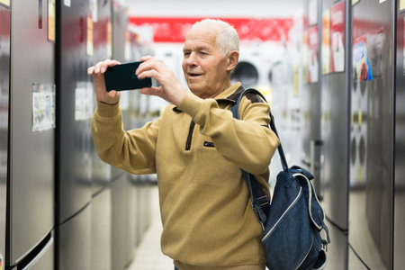 Senor man pensioner scanning QR of fridge in showroom of electrical appliance store