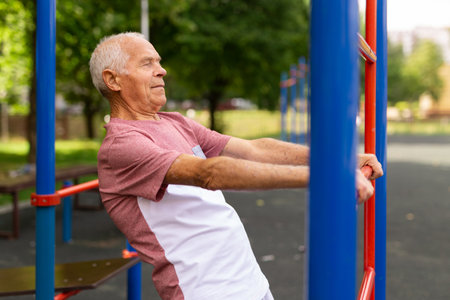 Sportive elderly man doing street fitness on the simulator in park