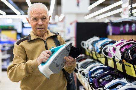 Senor man pensioner buying iron in showroom of electrical appliance storeの写真素材