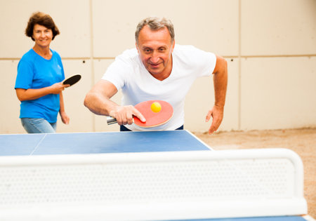 Happy mature man and woman playing table tennisの写真素材