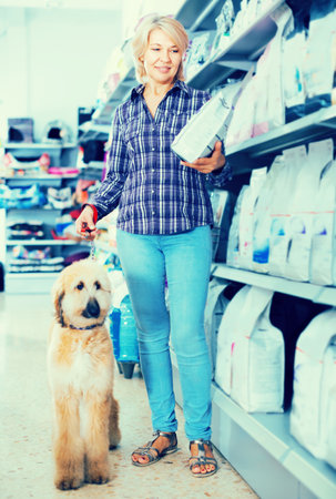 Female with Afghan Shepherd puppy choose pet food in storeの写真素材
