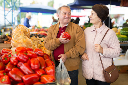 Mature married couple in casual clothes choosing organic bell peppers during date at local grocery marketの写真素材