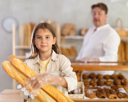 Portrait of little female customer holding bread in his hands in private bakeryの写真素材