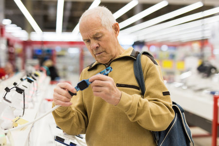 Elderly man examines smart watch in showroom of electronics storeの写真素材