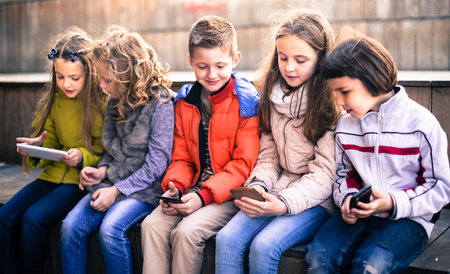 Children playing in smartphones on street bench in parkの写真素材