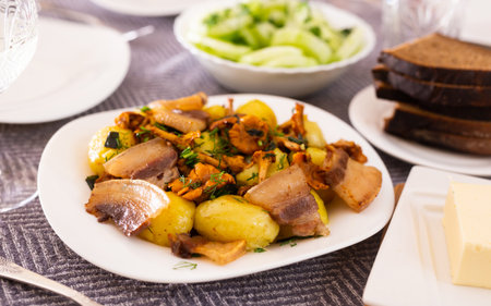 Baked potatoes with chanterelles and bacon served with herbs on white plateの写真素材