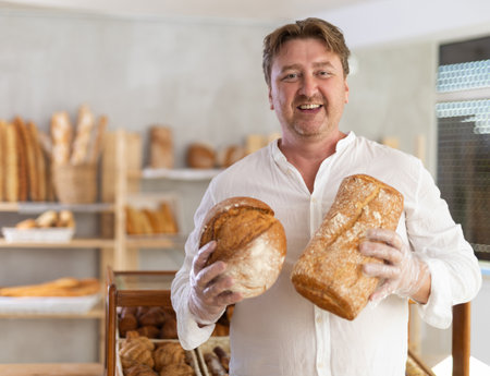 Man customer holding loaf of bread and baguettes with hands in disposable gloves.