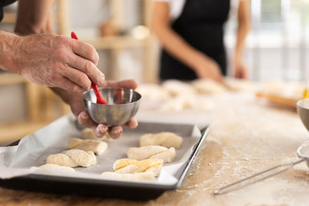 Close up of baker hands brushing uncooked dough pieces on baking sheet with oil before baking in...