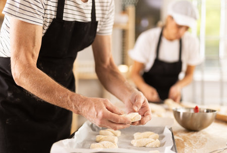 Bakers hands fold pieces of dough on baking sheetの写真素材