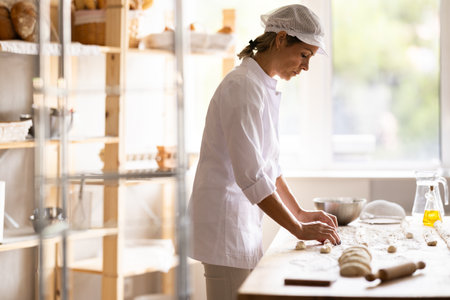 Female baker rolls dough into long sausages to be cut into pieces for baking buns