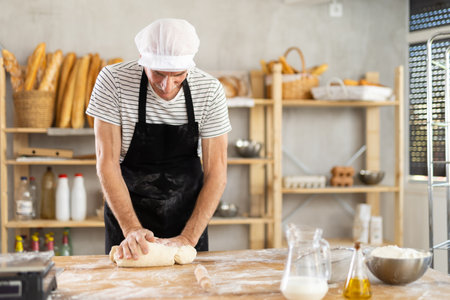 Elderly man kneads dough in bakeryの写真素材