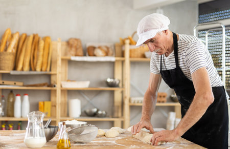 Elderly man baker rolls out dough