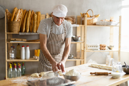 Elderly man kneads dough in bakery