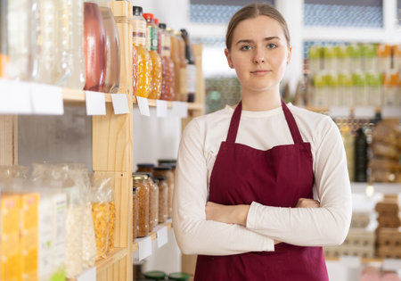 Portrait of female seller in an apron behind the counter of grocery storeの写真素材