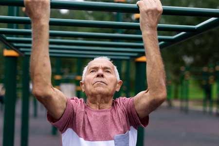Grandfather moves with his hands on a horizontal ladder on a sports ground