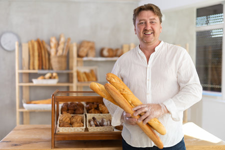 Man customer holding loaf of bread and baguettes with hands in disposable gloves.