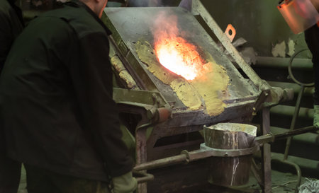 Workers at metallurgical plant pour molten metal from furnace into foundry ladle