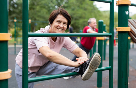 Elderly woman doing stretching exercises on the parallel bars at an outdoor sports ground