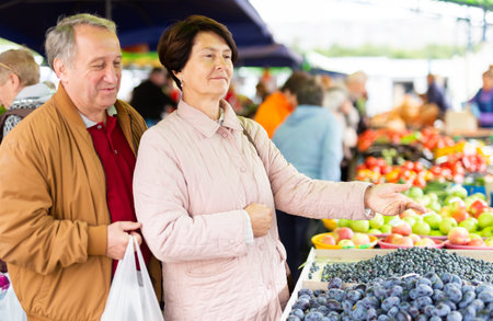 Elderly man and woman buy plums at an open marketの写真素材