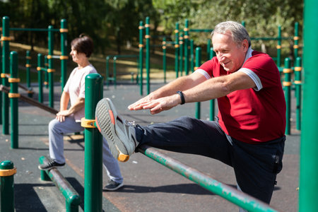 Elderly man doing stretching exercises on a sports bar at an outdoor sports groundの写真素材
