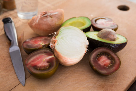 Vegetables black tomatoes, avocado and onions on wooden boardの写真素材