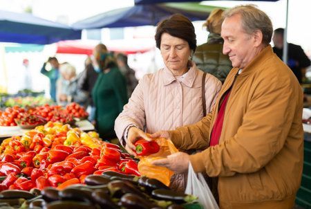 Aged man and woman customers buying pepper in open-air marketの写真素材