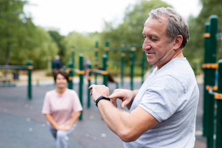 Elderly man looking at his smart bracelet in open-air sports areaの写真素材
