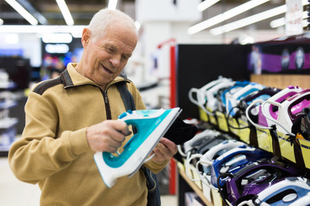 Senor man pensioner buying iron in showroom of electrical appliance storeの写真素材